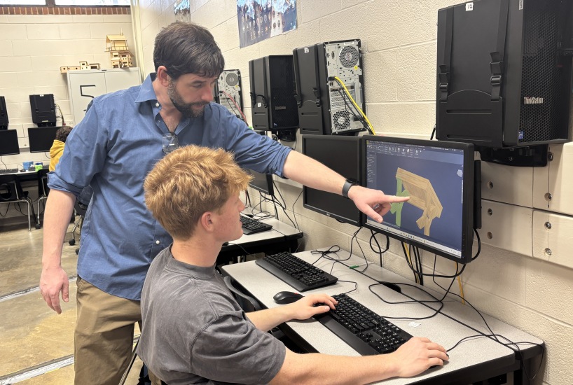 Turpin teacher points at a student's computer monitor as they work on an engineering project